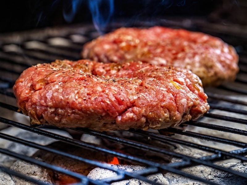 Ein roher Burger-Patty auf einem Grill von der Seite fotografiert.
