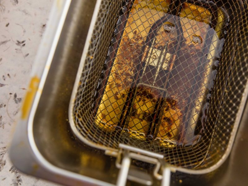 Eine Fritteuse mit altem Fett und darin hängendem Frittierkorb. Alles direkt von oben fotografiert.