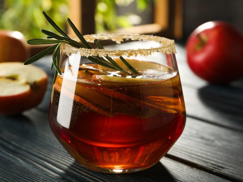 Ein Glas mit dem herbstlichen Aperol Spritz auf einem dunklen Holztisch von der Seite fotografiert.