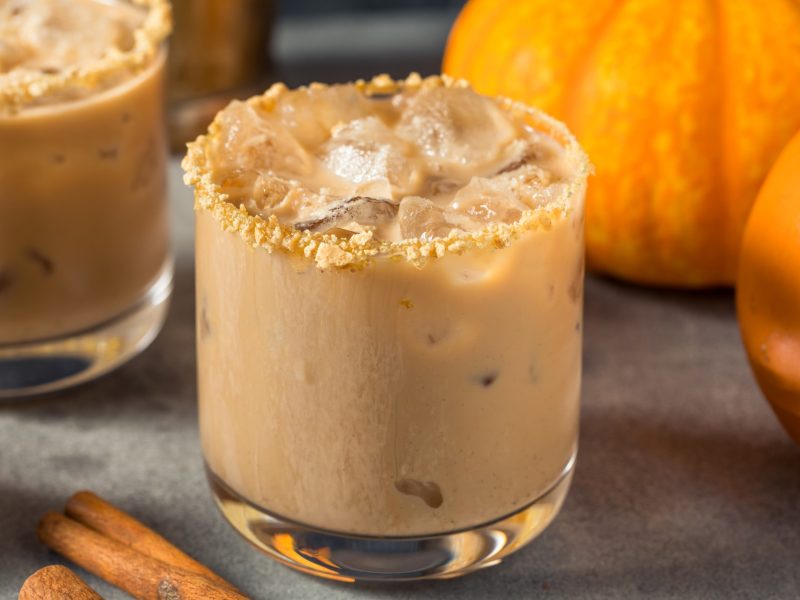 Pumpkin Spice White Russian mit Butterkeksrand in einem Glas, im Hintergrund Kürbisse.