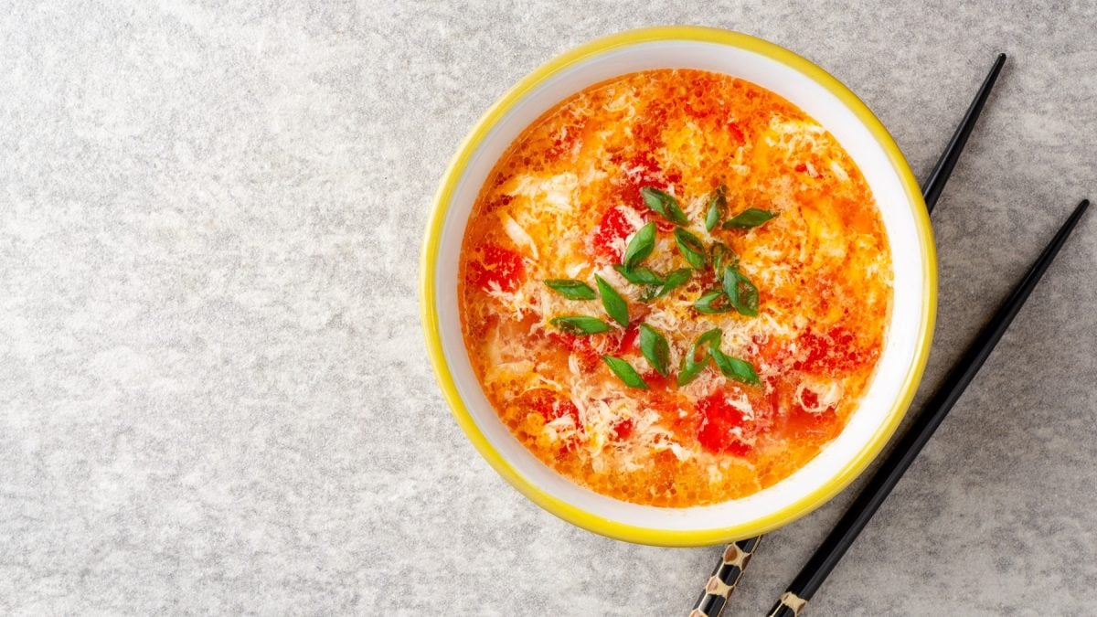 Eine gelbe Schale mit der Suppe auf einem grauen Untergrund mit schwarzen Stäbchen. Alles direkt von oben fotografiert.