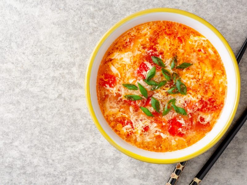 Eine gelbe Schale mit der Suppe auf einem grauen Untergrund mit schwarzen Stäbchen. Alles direkt von oben fotografiert.