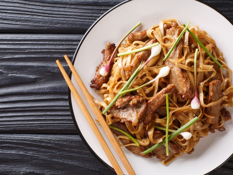 Ein weißer Teller mit dem Chow Fun auf einem schwarzen Holztisch.