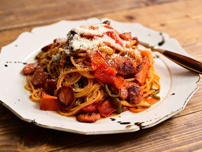 Ein Teller mit Spaghetti mit istrischem Wurstgulasch serviert auf rustikalem Holztisch mit weißem Randteller.