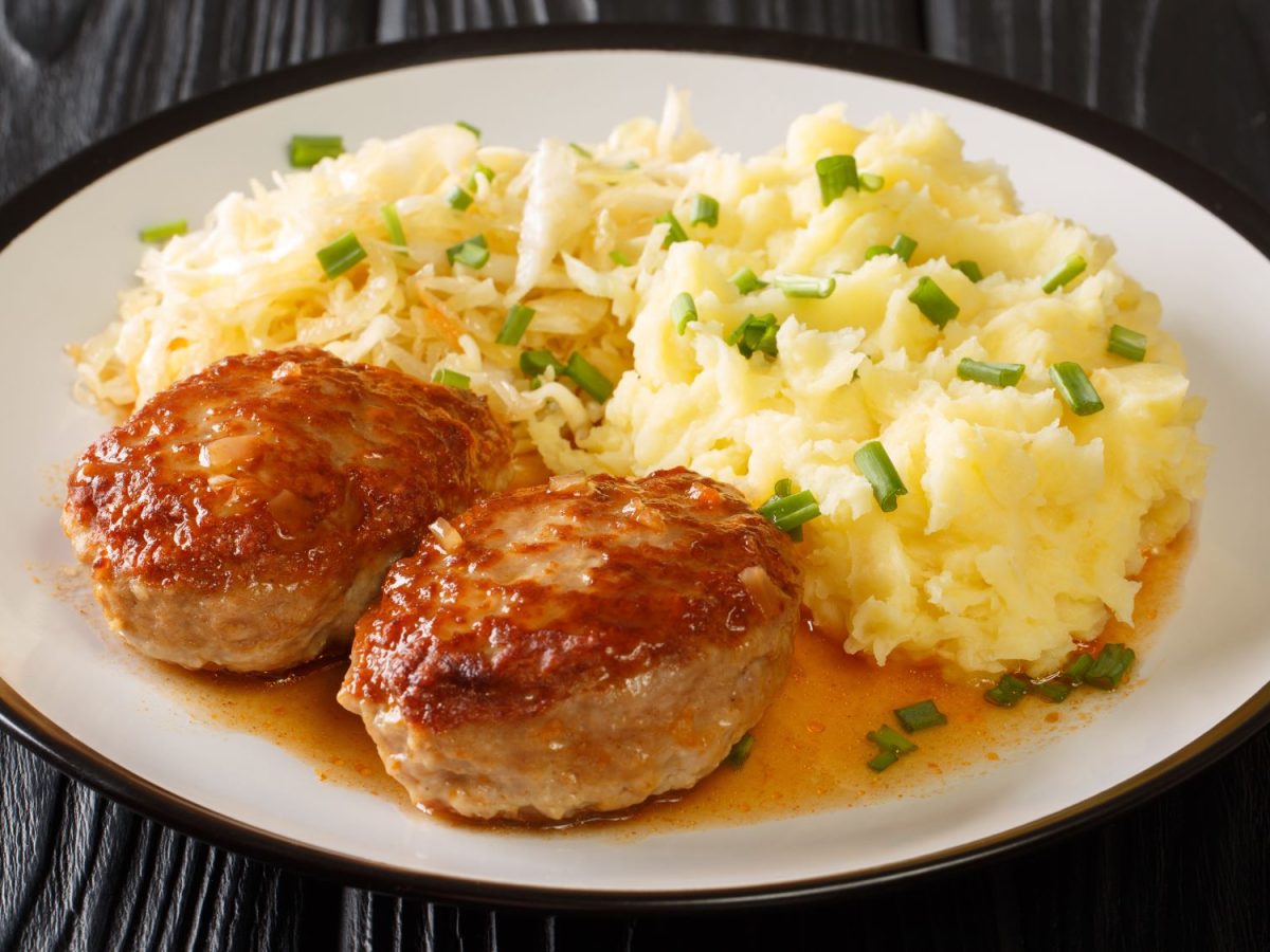 Ein Teller mit zwei Medisterkaker (norwegische Fleischklöße), serviert mit Kartoffelpüree und Sauerkraut. Das Gericht ist mit einer würzigen Soße und frischen Schnittlauchröllchen verfeinert.