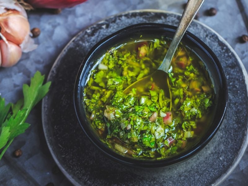 Ein graues Schälchen mit der grünen Kräutersauce auf einem grauen Tuch von oben fotografiert.