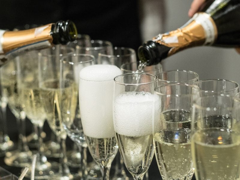 Frontal: Zwei Flaschen Sekt aus denen in leere Sektgläser eingeschenkt wird.