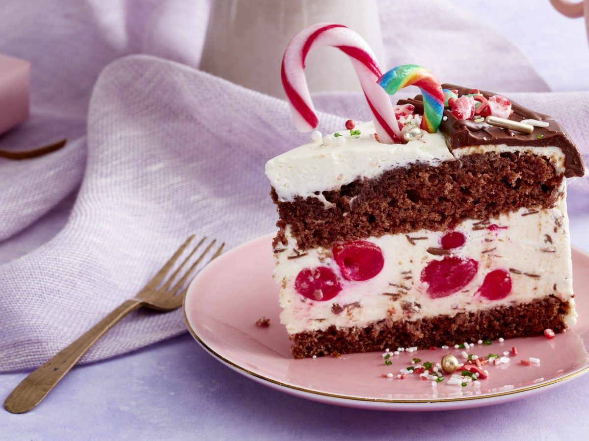 Ein Stück festliche Kirsch-Schmand-Torte mit Zuckerstangen drauf auf einem Teller mit hellem, festlichen Hintergrund.