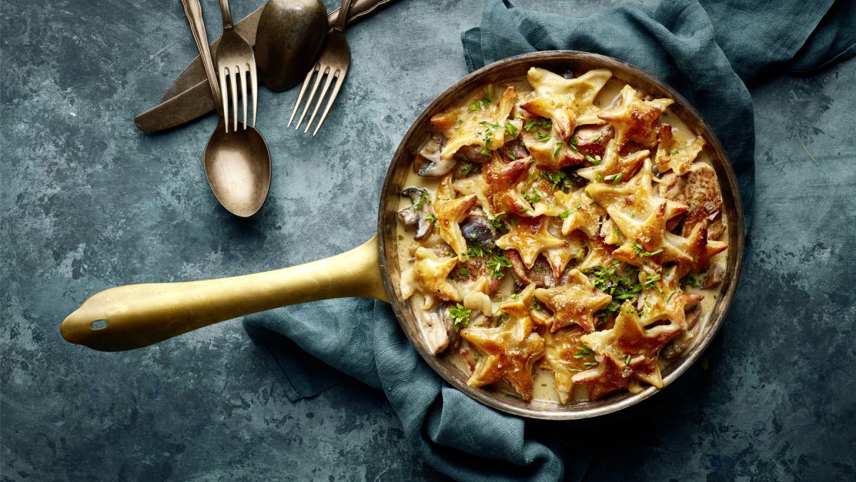 Draufsicht: Gebackenes Filettöpfchen mit Sternenhaube; Pfanne mit Fleisch und Pilzen in heller Sauce und gebackenen Blätterteig-Sternen darauf.