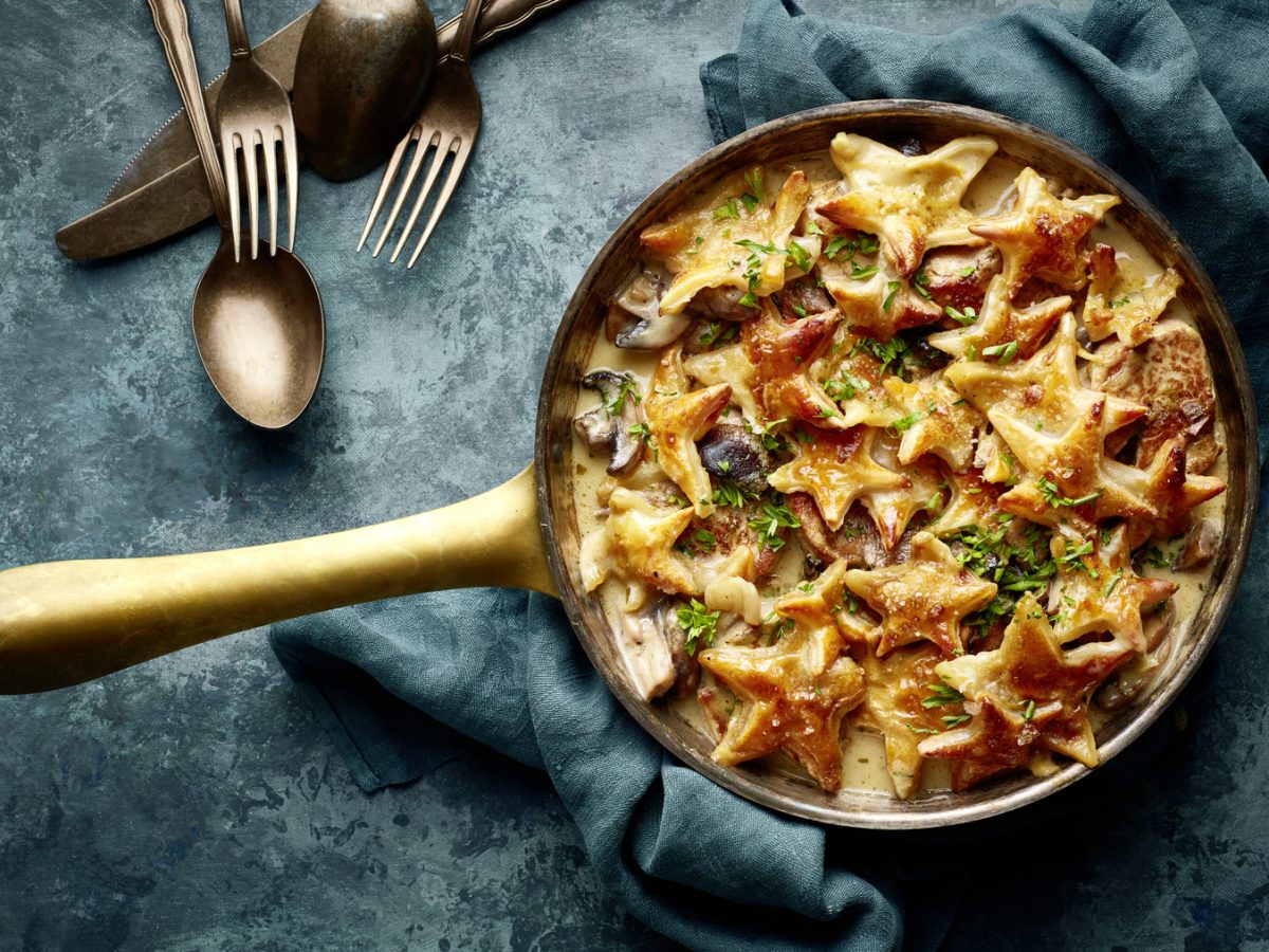 Draufsicht: Gebackenes Filettöpfchen mit Sternenhaube; Pfanne mit Fleisch und Pilzen in heller Sauce und gebackenen Blätterteig-Sternen darauf.