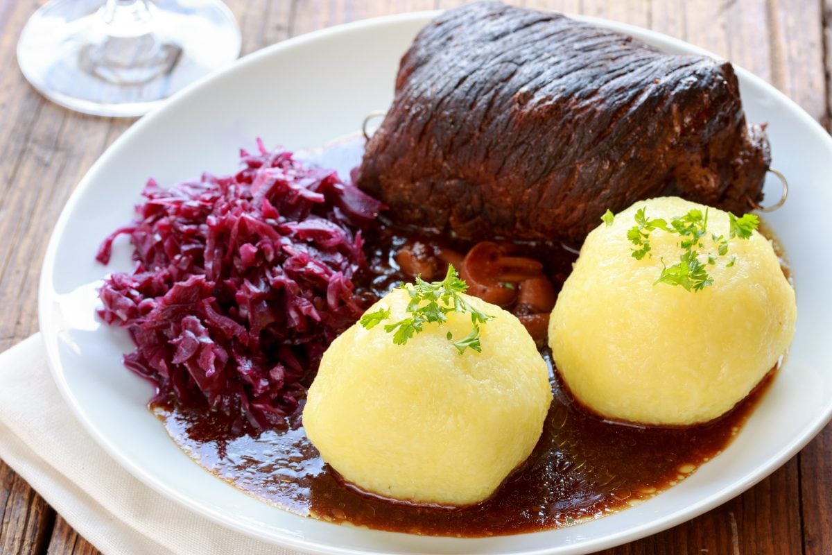 Ein Teller mit Braten, Rotkohl und gekochten Klößen in einer braunen Sauce auf einem weißen Teller.