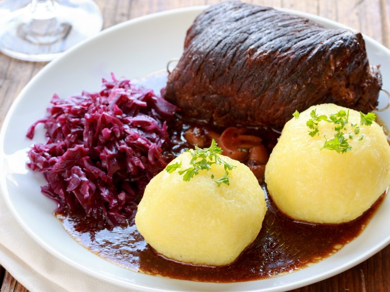 Ein Teller mit Braten, Rotkohl und gekochten Klößen in einer braunen Sauce auf einem weißen Teller.