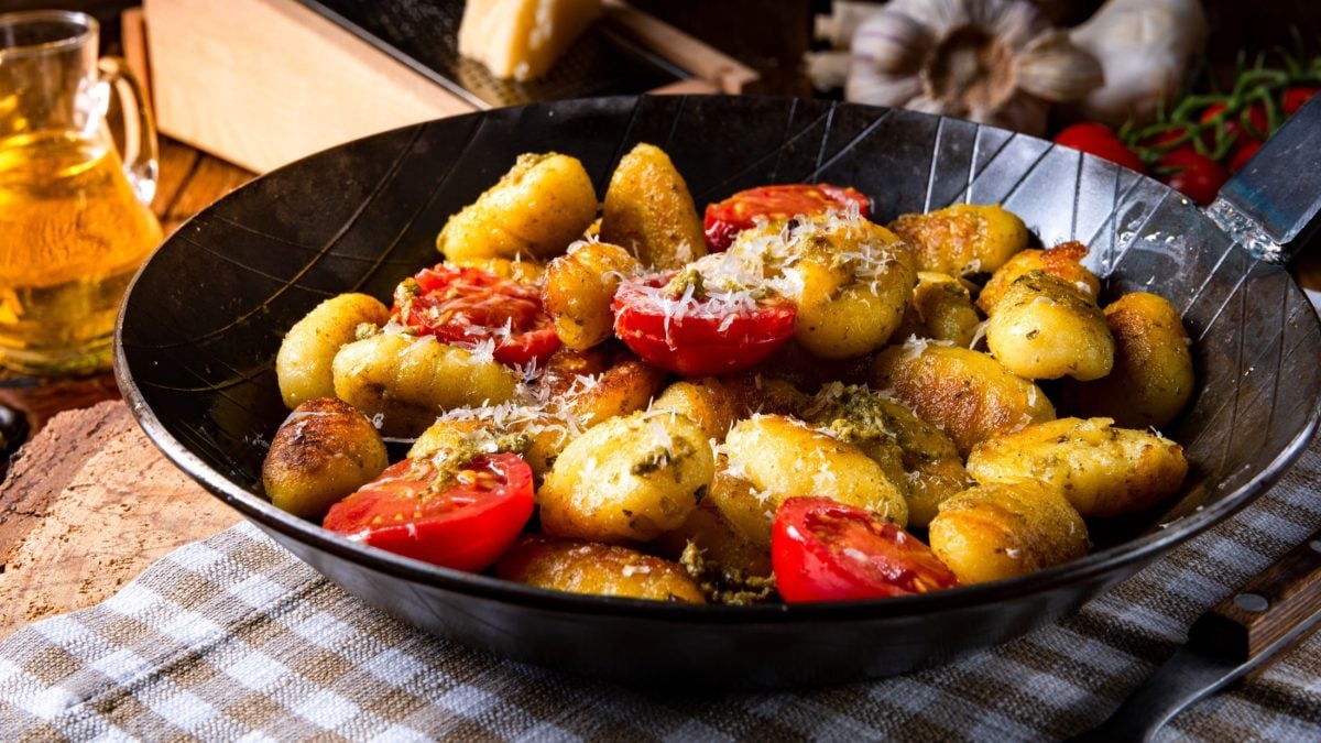 Eine Gnocchi-Pfanne mit Tomaten, Pesto und Parmesan auf einem rustikalen Untergrund.