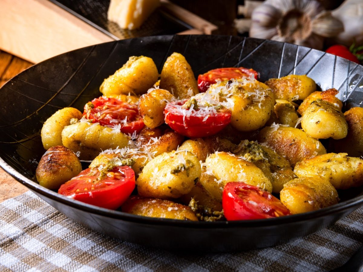 Eine Gnocchi-Pfanne mit Tomaten, Pesto und Parmesan auf einem rustikalen Untergrund.