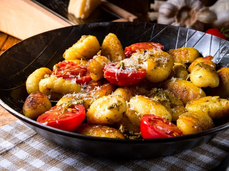 Eine Gnocchi-Pfanne mit Tomaten, Pesto und Parmesan auf einem rustikalen Untergrund.