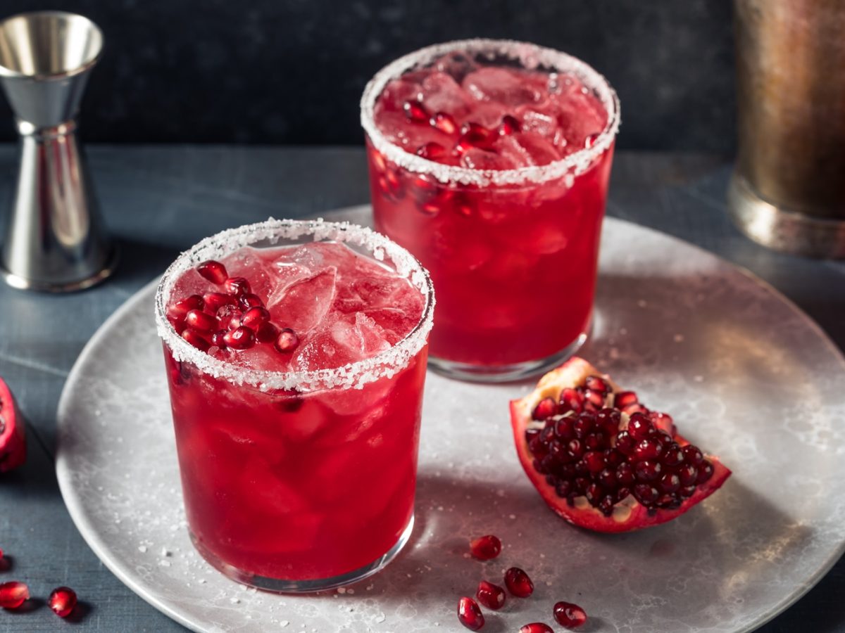 Zwei Gläser mit dem Granatapfel Paloma auf einem hellgraue Teller mit dunkelgrauem Untergrund. Alles von der Seite fotografiert.