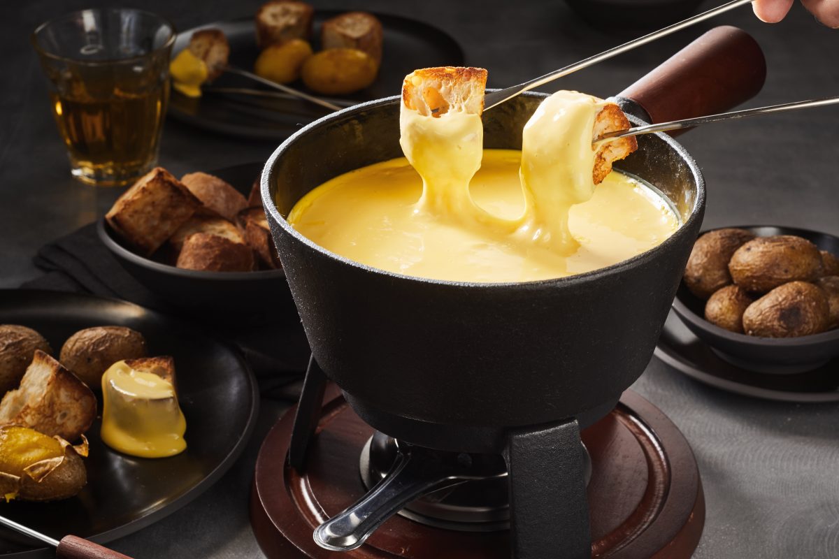 Käsefondue mit Brot vor dunklem Szenario.