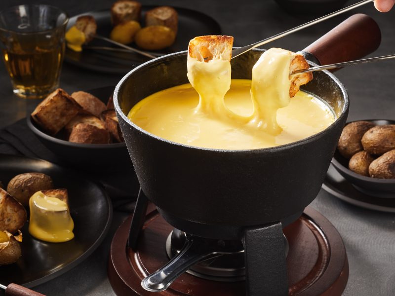 Käsefondue mit Brot vor dunklem Szenario.