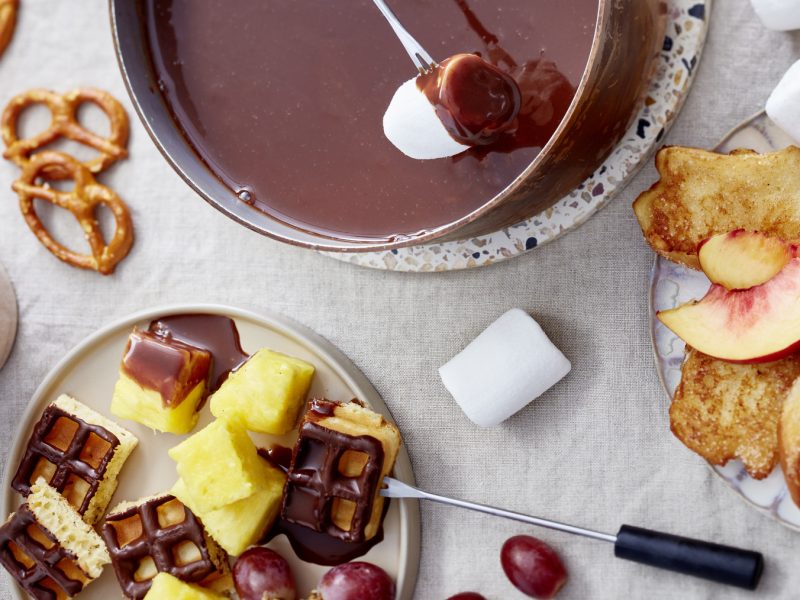 Draufsicht: In zwei Schalen Nougatfondue mit armen Ritterlein, drum herum Knusperbrezeln, Obst, Marshmallows und Mini-Waffeln