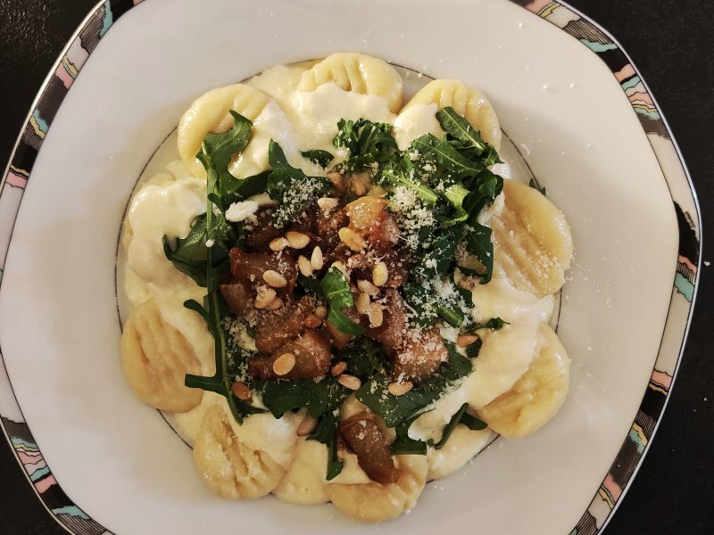 Gnocchi in cremiger Provolone-Sauce, garniert mit Rucola, karamellisierter Birne, Pinienkernen und Parmesan, angerichtet auf elegantem Porzellanteller.
