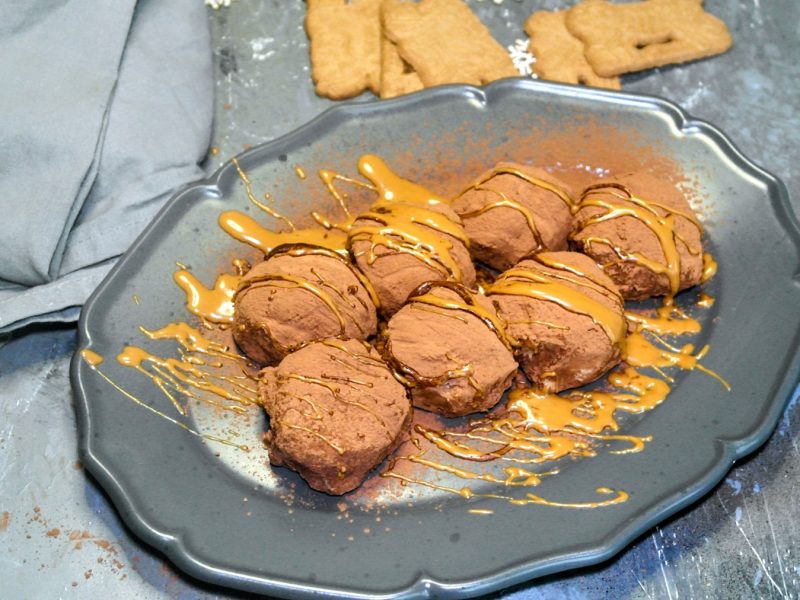 Ein grauer Teller mit den Tiramisu Bällchen auf einem grauen Steintisch mit Spekulatius im Hintergrund. Links daneben ein graues Tuch.