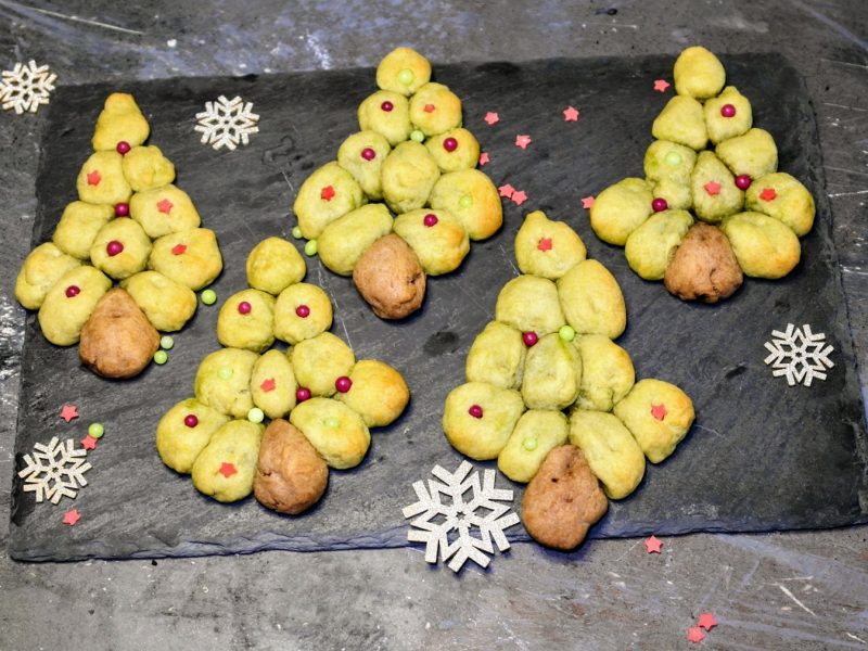 Ein eschwarze Schieferplatte mit den Cookies auf einem grauen Tisch mit weihnachtlicher Deko. Alles direkt von oben fotografiert.