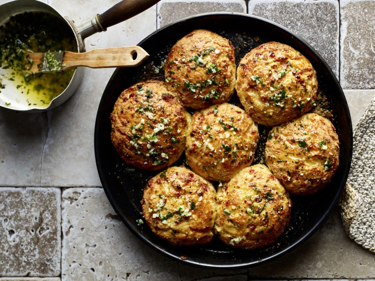Draufsicht: Triple-Cheese-Brötchen aus der Pfanne, daneben Knoblauchbutter mit Pinsel.