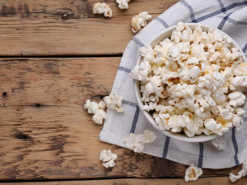 Trüffelpopcorn in einer weißen Schüssel auf einem Geschirrtuch auf hölzernem Hintergrund.