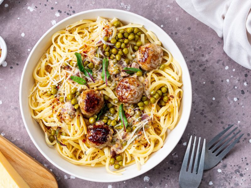 Wikinger-Pasta mit Fleischbällchen, grünen Erbsen, frischen Kräutern und geriebenem Parmesan, angerichtet in einer weißen Schale.