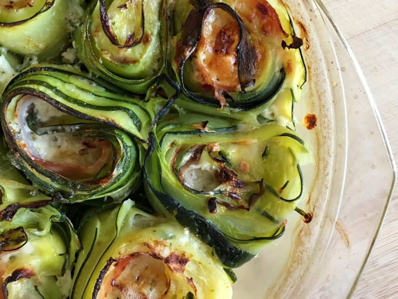 Zucchini-Röllchen gefüllt mit Käse und Schinken, überbacken mit Käse in einer runden, gläsernen Auflaufform.