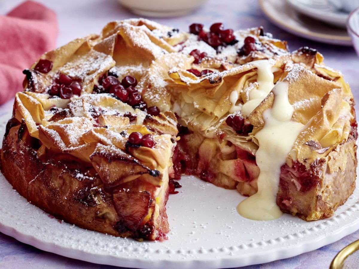 Angeschnittene Apfel-Strudel-Torte mit Vanillesauce auf Servierteller.
