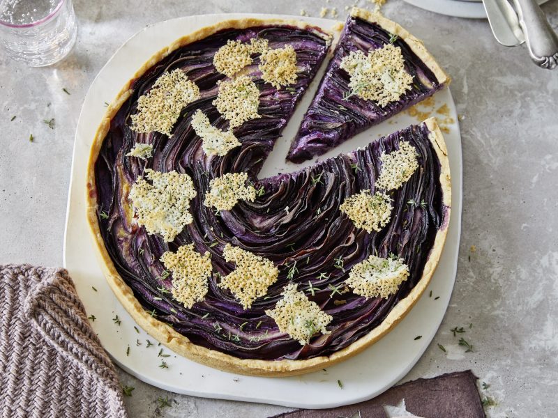 Die violette Möhren-Tarte mit Parmesanchips auf einem weißen Teller und grau-steinernem Untergrund. Alles direkt von oben fotografiert.