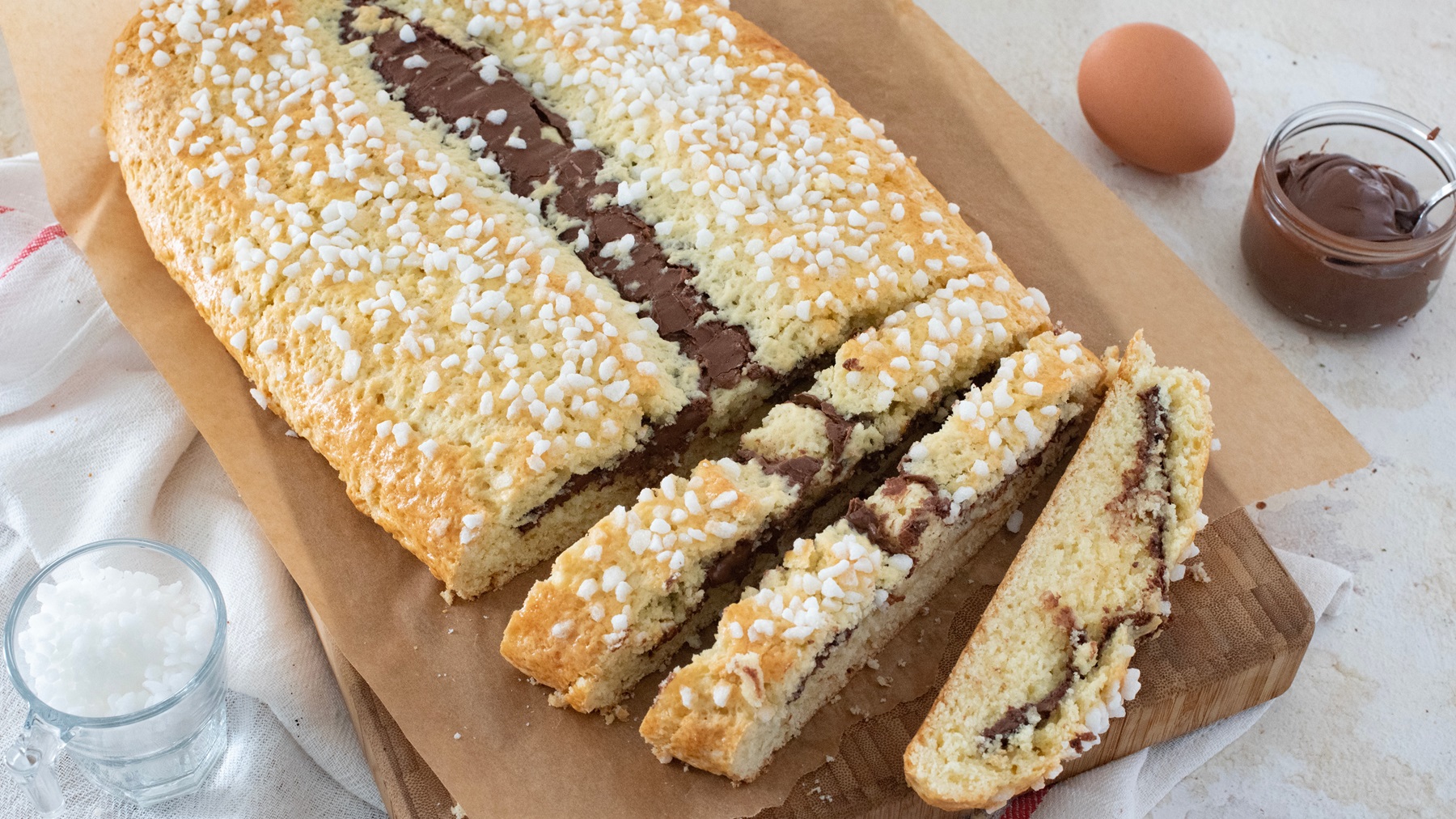 Frisch gebackener Bensone mit glänzender Schokofüllung und knusprigem Hagelzucker auf einem Holzbrett, umgeben von Zutaten.
