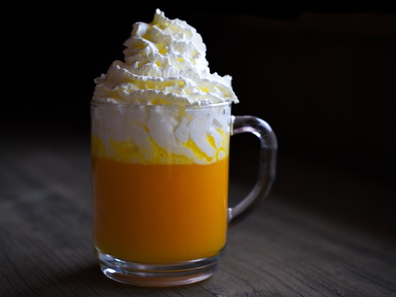 Ein Glas mit dem Bombardino auf einem dunklen Holztisch mit schwarzem Hintergrund. Alles sehr nah und recht zentral fotografiert.