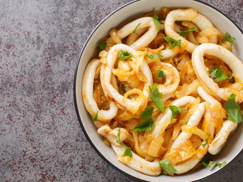 Draufsicht auf eine wei0ße Schüssel mit Calamares encebollados vor einem grauen Untergrund.