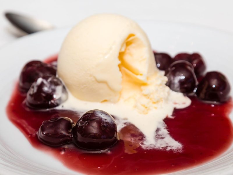 Cherries Jubilee mit Vanilleeiskugel und eingelegten Kirschen in süßer roter Sauce, serviert auf einem eleganten weißen Teller.