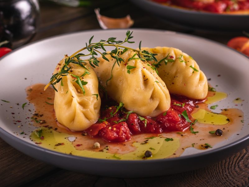 Ein grauer Teller mit den Teigtaschen und Tomatensauce auf einem Holztisch von schräg oben fotografiert.