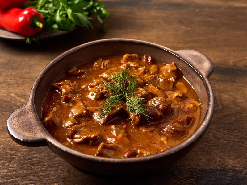 Draufsicht, schräg: Ein Topf Pfefferpotthast, eine Art Pfeffer-Ragout, auf einem Holztisch.