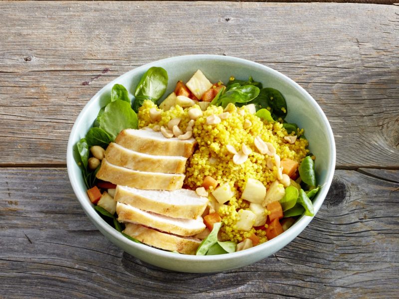 Quinoa-Hähnchen-Bowl in einer Schüssel auf hölzernem Hintergrund.