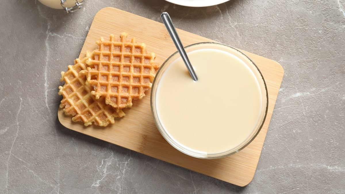 Ein kleines Schneidebrett mit der Waffelmasse und frisch ausgebackenen Waffeln auf grauem Untergrund. Alles direkt von oben fotografiert.