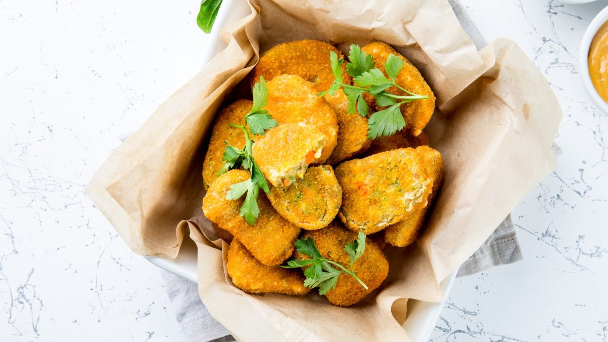 Gemüse-Nuggets in einer Schüssel mit Backpapier ausgelegt auf hellem, marmoriertem Hintergrund.