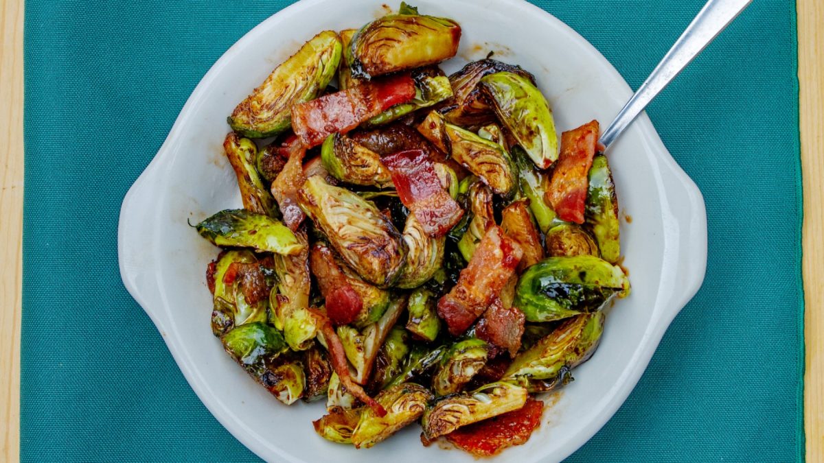Gochujang Rosenkohl mit Speck in einer weißen Schüssel auf einem blauen Tuch.