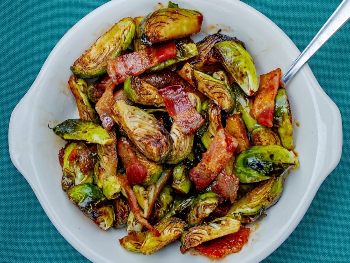 Gochujang Rosenkohl mit Speck in einer weißen Schüssel auf einem blauen Tuch.