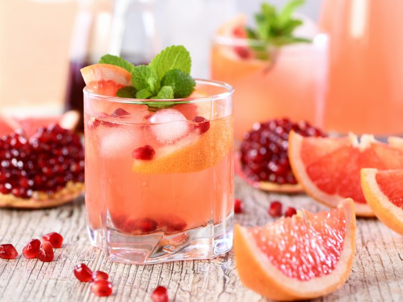 Grapefruit Tequila Smash mit Grapefruit, Granatapfelkernen und Minze in einem klaren Glas, arrangiert auf rustikalem Holzhintergrund mit frischen Früchten.
