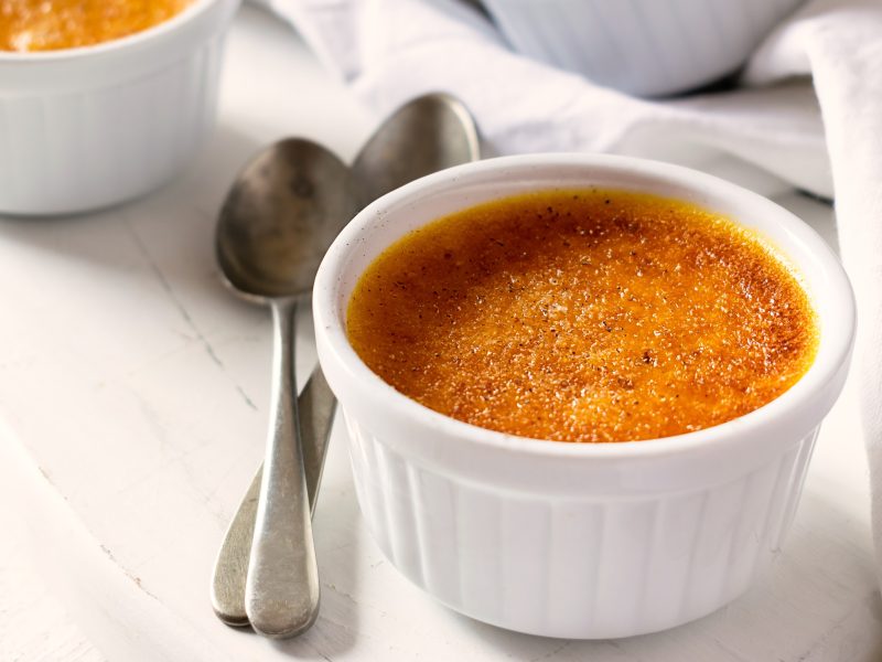 Zwei weiße Schalen mit der Kürbis Crème brûlée auf einem hellen Tisch von schräg oben fotografiert.