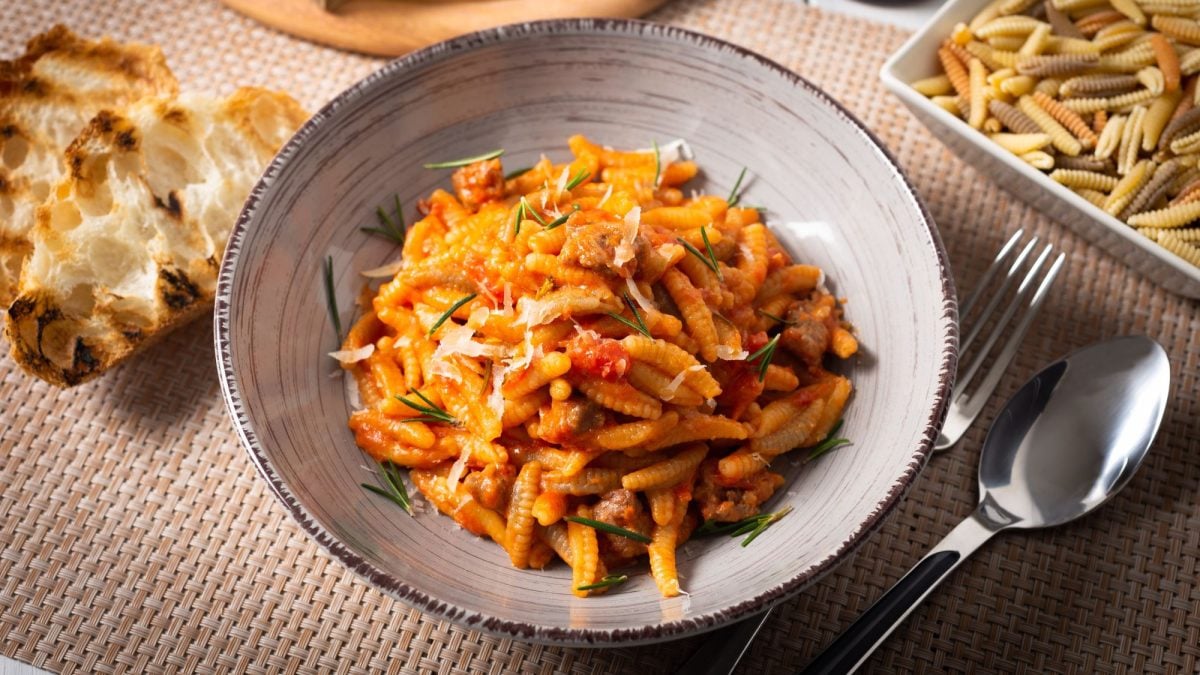 Rustikale Malloreddus alla campidanese mit kräftiger Tomatensauce, garniert mit Rosmarin und geriebenem Käse, daneben gegrilltes Brot.