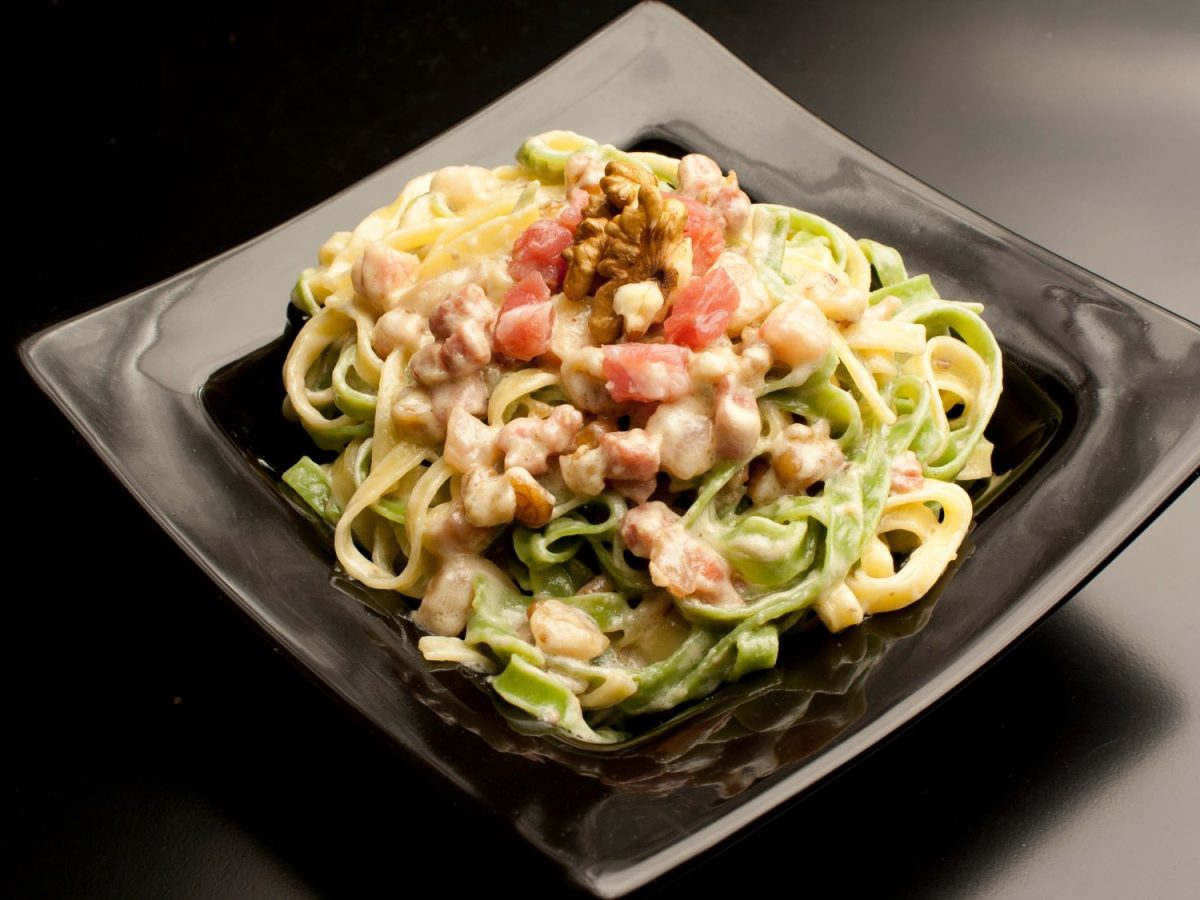 Paglia e fieno – zweifarbige Pasta mit Pancetta und Walnüssen auf schwarzem Teller, edel angerichtet mit einer cremigen Sauce.