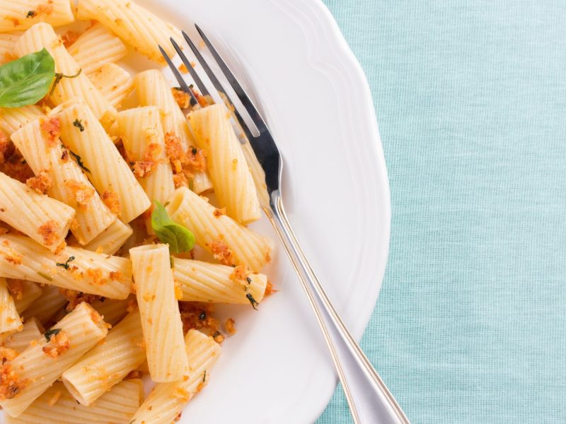 Rigatoni mit Pangritata bestreut auf weißem Teller.
