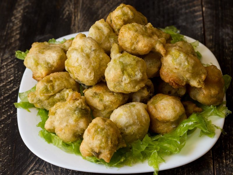 Köstlich knusprige Zeppoline di alghe in goldener Panade, serviert auf grünem Salatbett, präsentiert auf einem dunklen Holztisch.