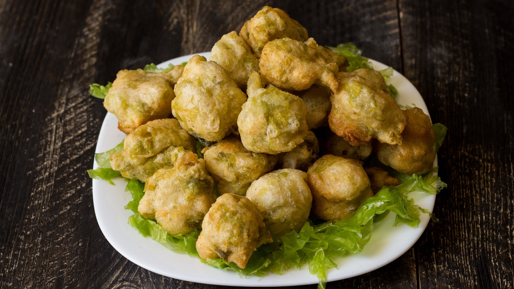 Köstlich knusprige Zeppoline di alghe in goldener Panade, serviert auf grünem Salatbett, präsentiert auf einem dunklen Holztisch.